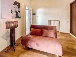 Un dormitorio con una cama, una lámpara de pie, un radiador y una puerta que da a otra habitación.