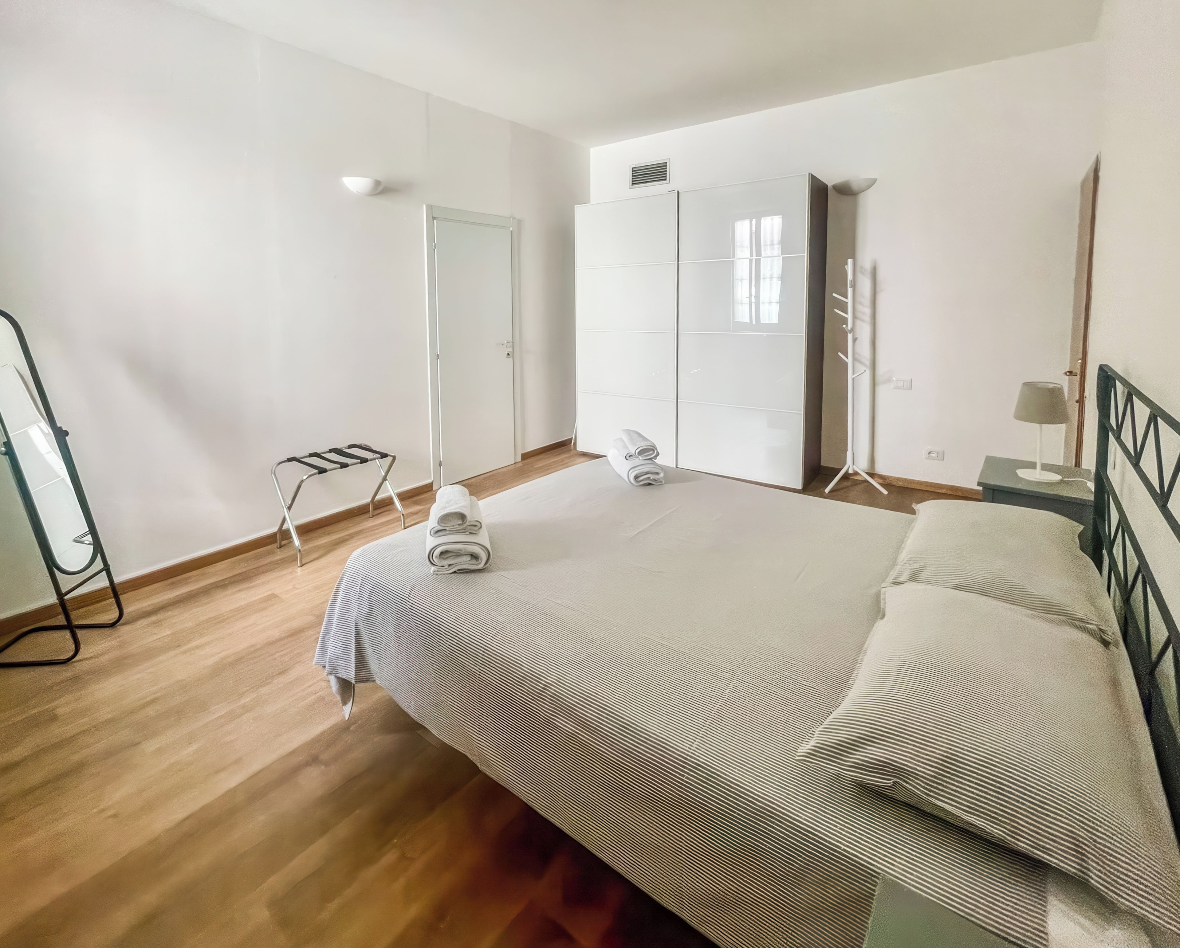 Un dormitorio con cama, armario, espejo y radiador.