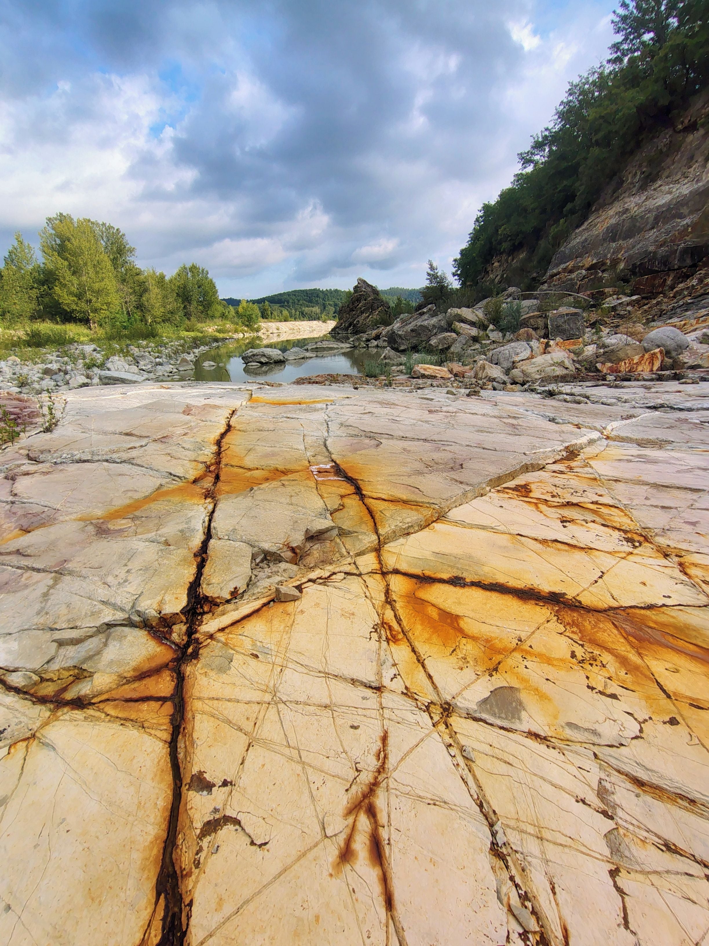 A natural landscape with a riverbed, rocks, and trees.