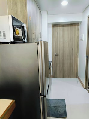 A compact kitchen with a refrigerator, microwave, and cabinets. - Coast Residences (Pasay City)