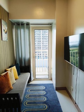 A hotel room with a sofa, a television, a patterned rug, and a view through a door. - Coast Residences (Pasay City)