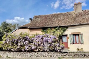 Ein Gebäude mit einem Stehdach, einer roten Tür und einem Garten mit violetten Blütenpflanzen.