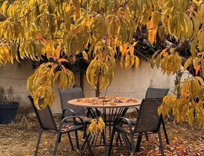 An outdoor seating area with a round table and chairs, surrounded by trees with yellow leaves. - La Parenthèse Suryssoise: Sit down, take a breath... Near Sancerre and the Loire River (Sury-ès-Bois)