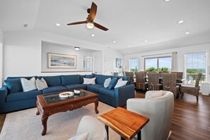 Ein geräumiges Wohnzimmer mit einem blauen Ecksofa, einem Holztisch und einem Deckenventilator.