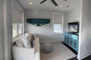 A room with a white sofa, teal accent wall, a television, and a ceiling fan. - NEW Seaglass Villa | Golf Cart + 5 Bikes | 30A (Santa Rosa Beach)