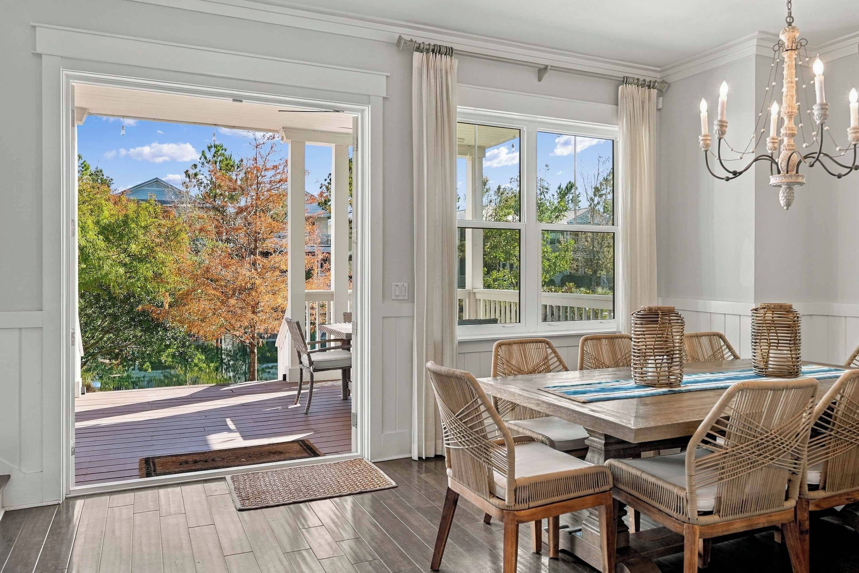 A dining area with a table and chairs, a chandelier, and a view of trees and a house through large windows.
