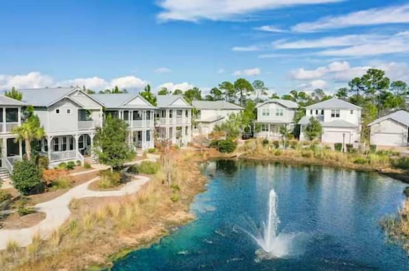 A residential area with houses along a body of water, a visible fountain, and a clear sky. - NEW Seaglass Villa | Golf Cart + 5 Bikes | 30A (Santa Rosa Beach)