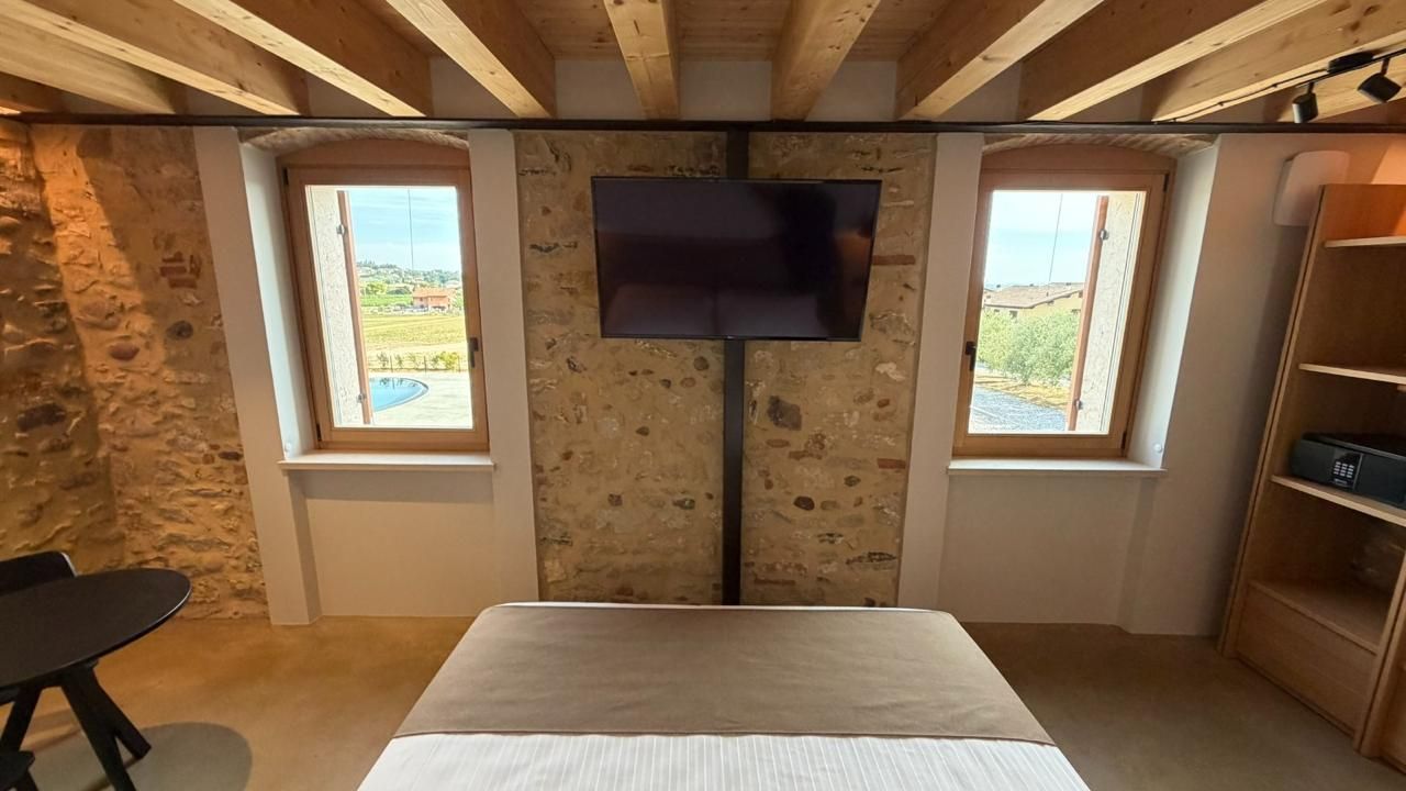 A room with a bed, a TV, and two windows with a view.