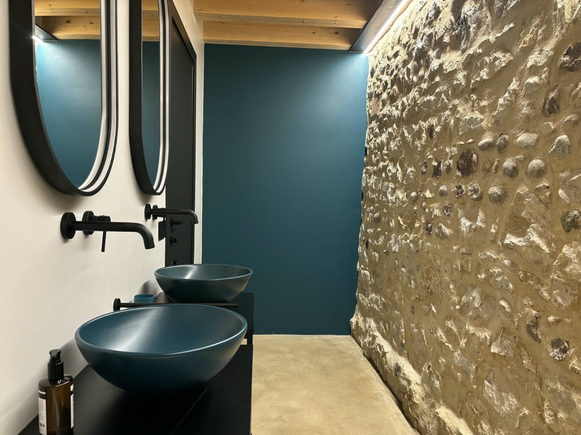 A bathroom with a modern design, featuring a black countertop, two blue bowls, a black faucet, and a mirror.