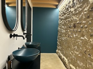 Un baño con diseño moderno, que incluye un mostrador negro, dos lavamanos azules, un grifo negro y un espejo.