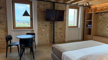 Una habitación con cama, televisor montado en la pared, mesa con sillas y ventana con vistas.