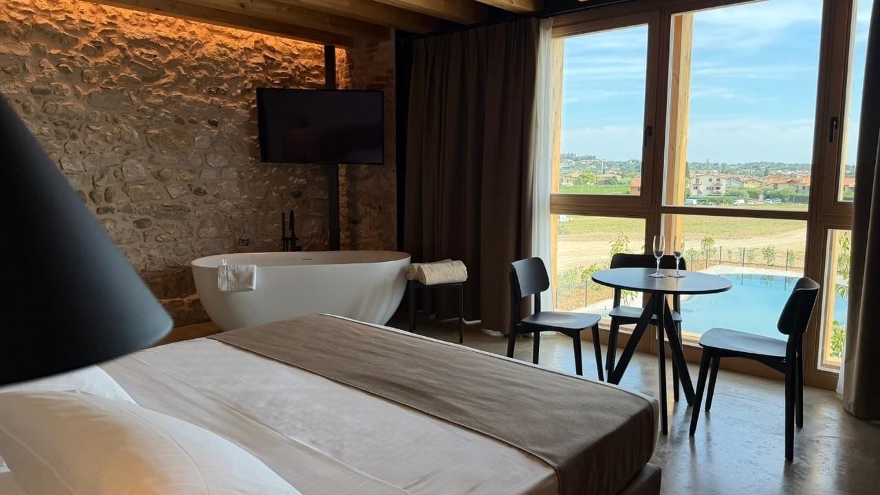 Habitación de hotel con cama, televisor, mesa y sillas, y vista a una piscina.