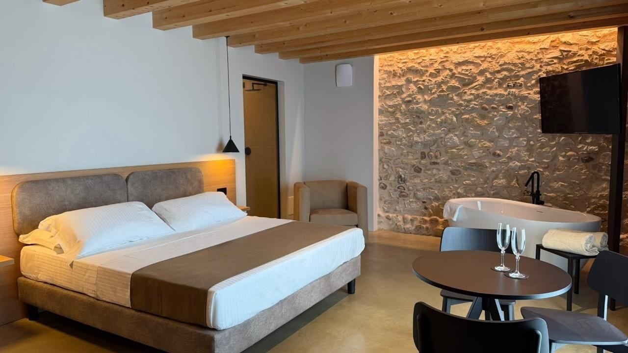 Ein Schlafzimmer mit einem Bett, einem Sessel, einem runden Tisch mit Gläsern und einer Steinwand.