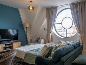 Quarto moderno com uma cama grande, televisão de tela plana, janela com cortinas e vista para edifícios.