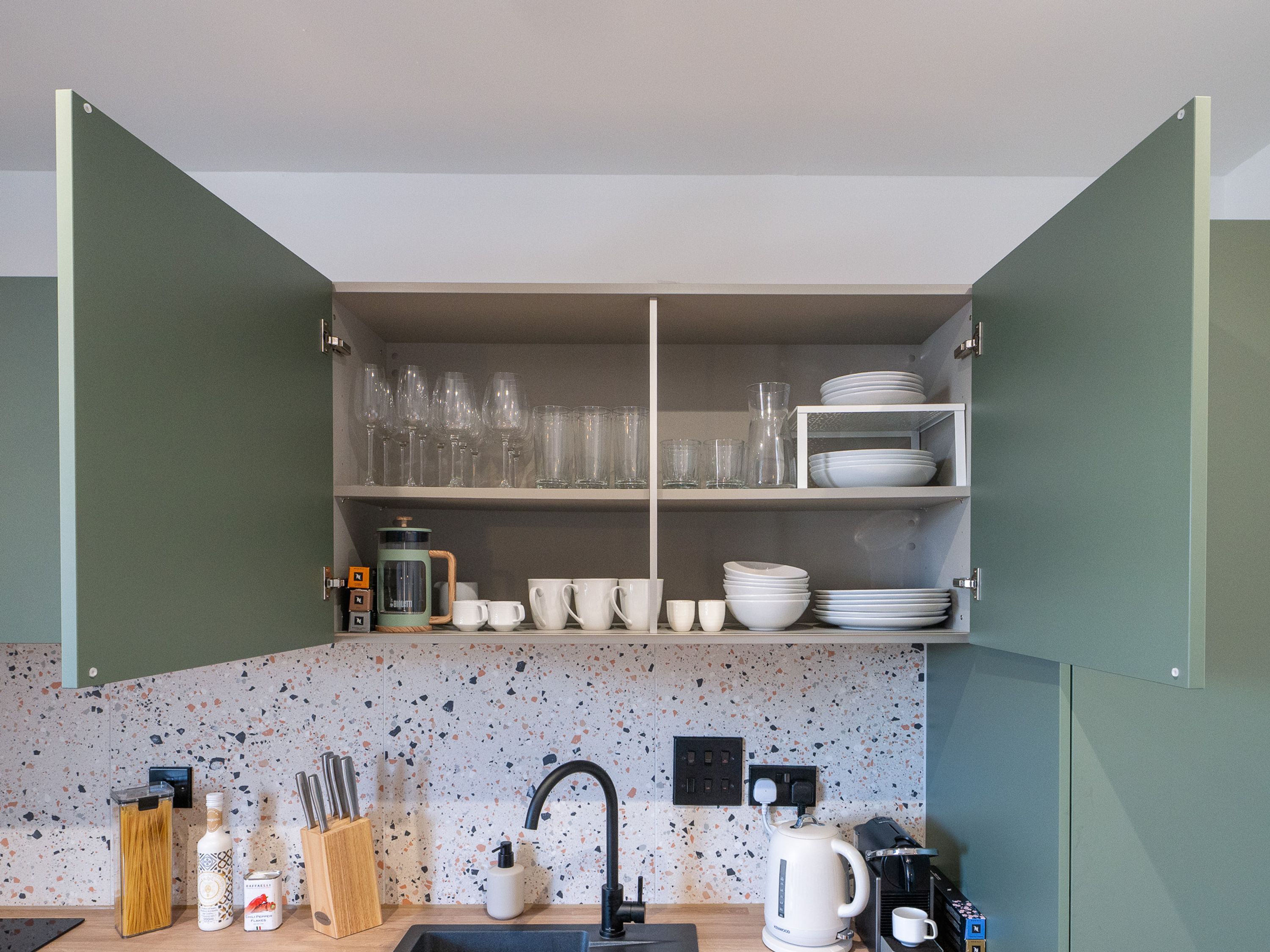 A kitchen with open cabinets displaying glassware, plates, and a coffee maker.