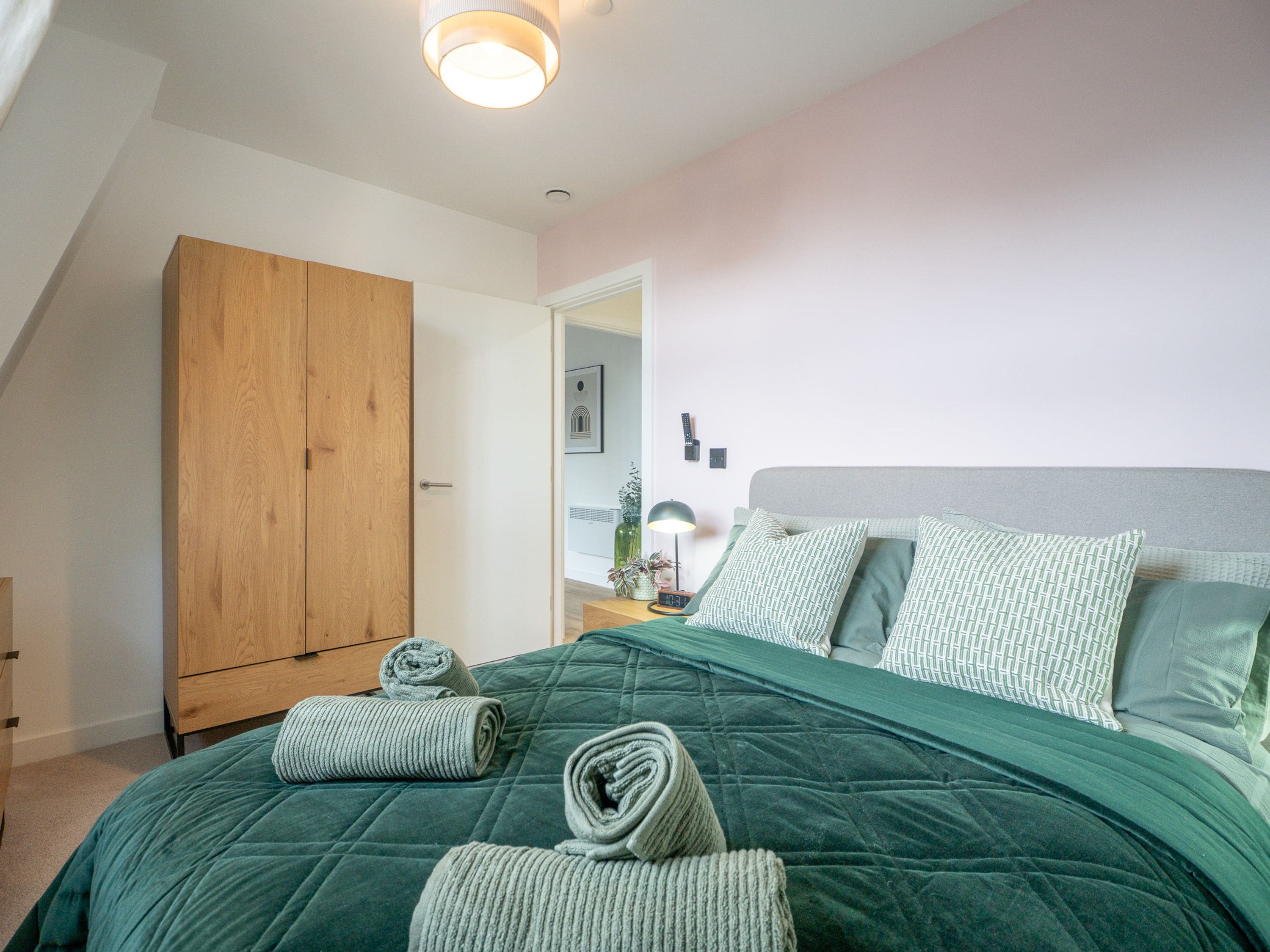 A bedroom with a bed, a wooden wardrobe, a nightstand with a lamp, and a wall-mounted clock.