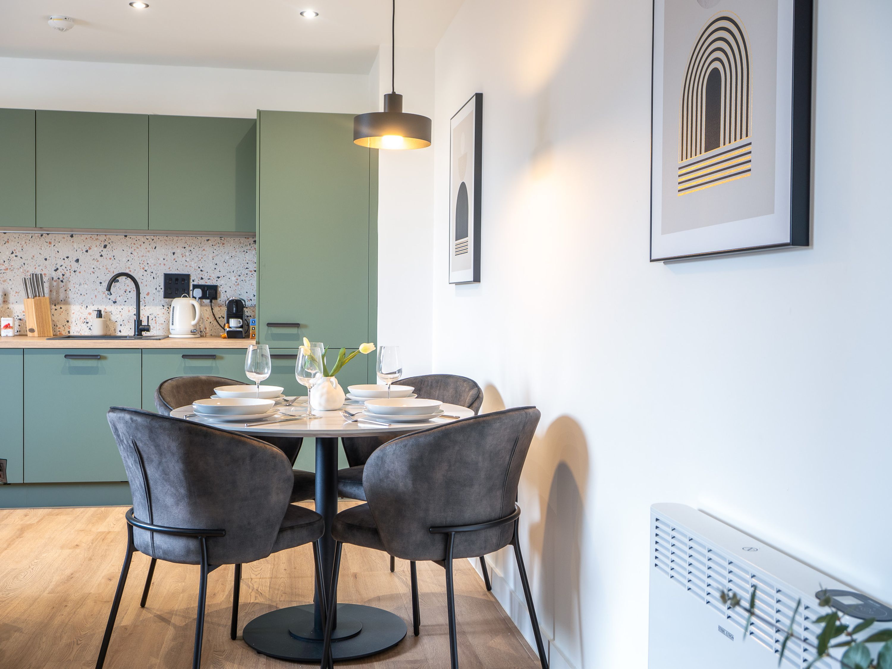 A modern kitchen with green cabinets, a dining table set for four, and a pendant light above.