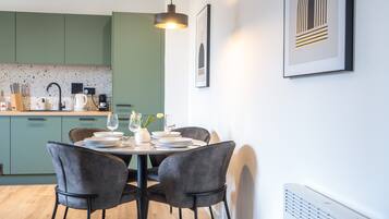 A modern kitchen with green cabinets, a dining table set for four, and a pendant light above.