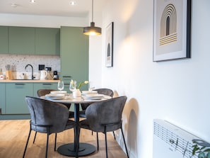 Uma cozinha moderna com armários verdes, uma mesa de jantar posta para quatro pessoas e uma luminária pendente.