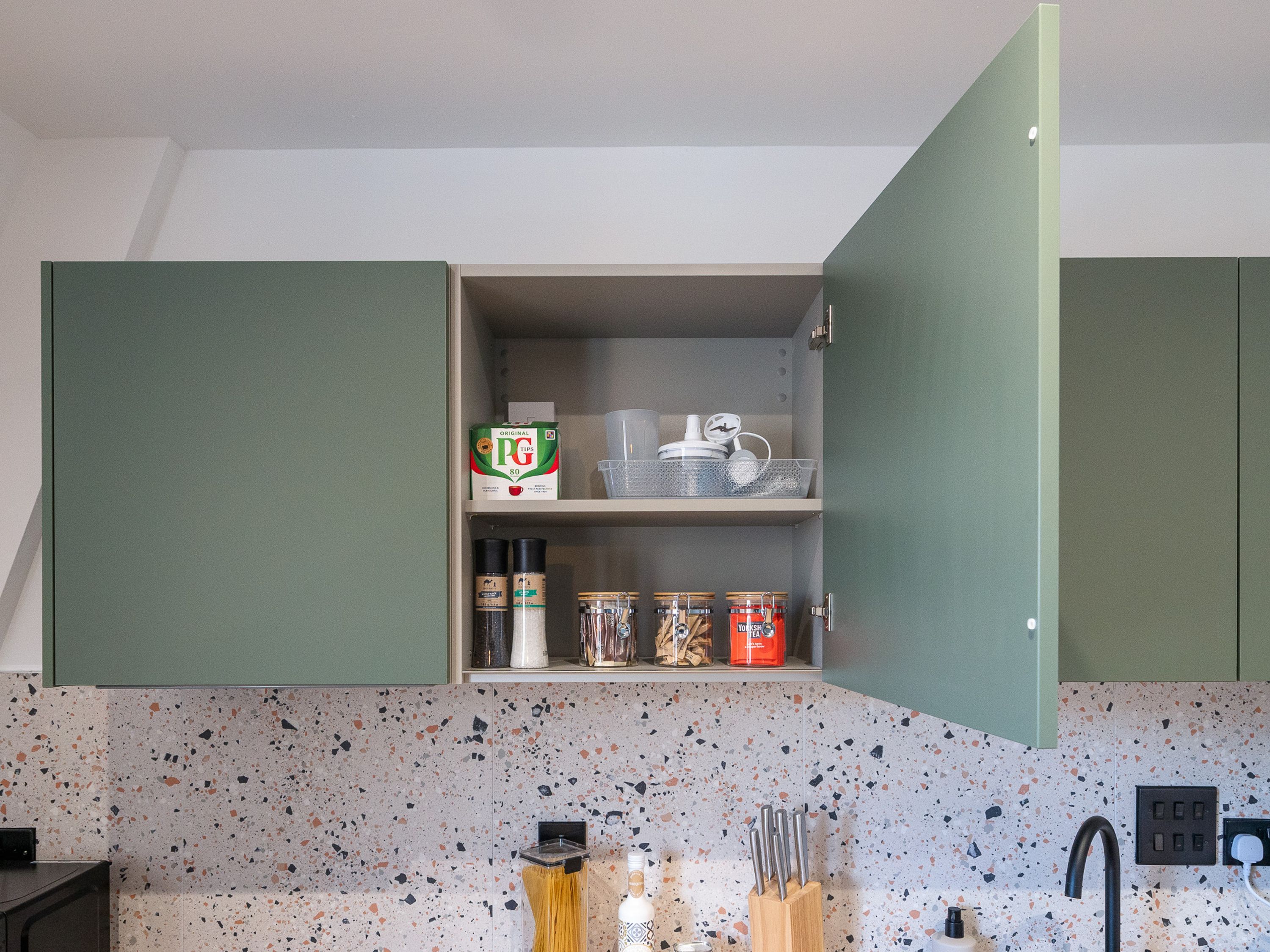 Eine Küche mit gefleckter Spritzschutzwand, einer Arbeitsplatte mit Geschirr und einem Schrank mit Aufbewahrungsmöglichkeiten.