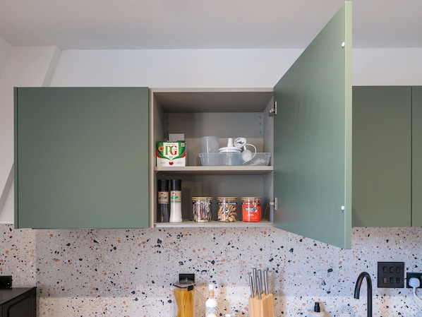 Uma cozinha com revestimento salpicado, bancada com utensílios e armário com objetos para guardar.