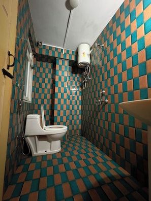 A bathroom with a checkered floor pattern, a toilet, a sink, and a shower. - Travel Pickle (Darjeeling)