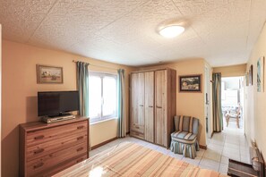 A bedroom with a television on a dresser, a wardrobe, a striped chair, and a view of a balcony. - Vrbo Property (Beaussais-sur-Mer)