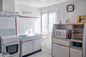 Eine Küche mit Herd, Spüle und Mikrowelle. An der Wand hängt eine Uhr und das Fenster ist mit Vorhängen versehen.