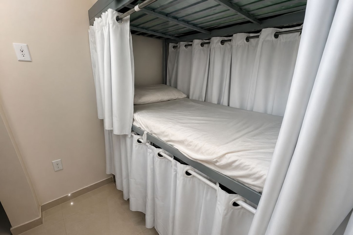 A bunk bed with white bedding and curtains, a metal ceiling, and a tiled floor.