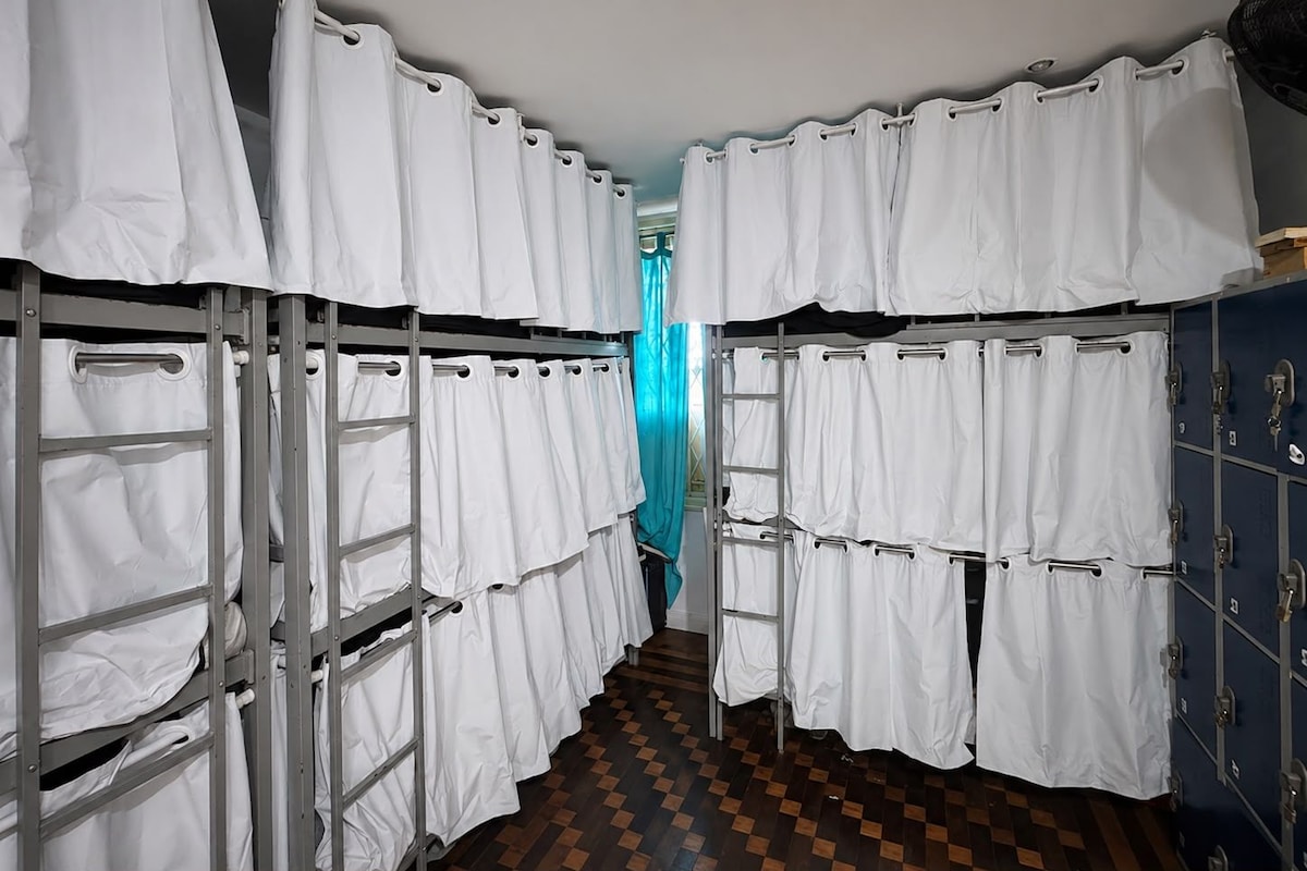 A corridor with bunk beds and lockers, a checkered floor, and a blue curtain.