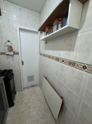 A kitchen with white tiled walls, a white door, and a white radiator. There are shelves above the door with containers. - 3min da Praia de Copacabana (Rio de Janeiro)