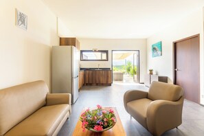 A modern living room with a sofa, a coffee table with flowers, a kitchen with wooden cabinets, and a view through the door. - Casa Pasha - Apartment Sasha - Jan Thiel (Jan Thiel)