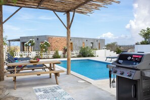 A poolside area with a barbecue grill, a wooden table, and a bench. - Casa Pasha - Apartment Sasha - Jan Thiel (Jan Thiel)