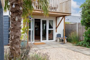 Ein Wohnhaus mit überdachter Terrasse, Holzdeck und Gartenanlage mit Kies und Pflanzen.