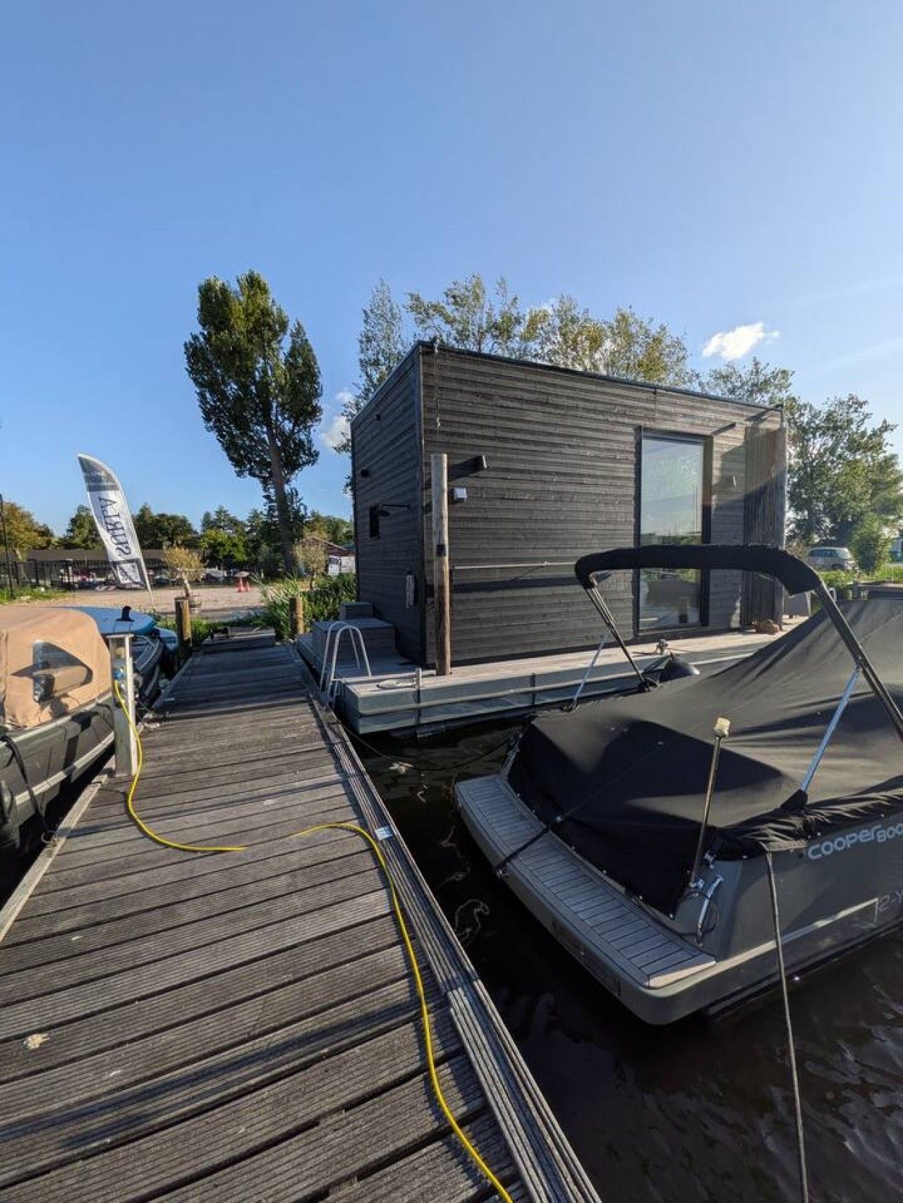 A modern, compact boat house with a small deck area, a covered boat, and a visible flag.