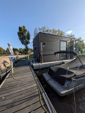 A modern, compact boat house with a small deck area, a covered boat, and a visible flag.