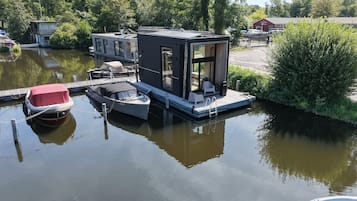 Una casa flotante amarrada en una masa de agua tranquila, rodeada de vegetación y un cielo despejado.