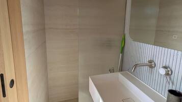 Un baño moderno con ducha, un lavamanos blanco y un espejo.