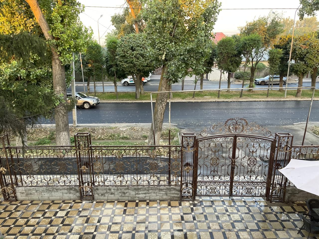 A terrace with a tiled floor, a wrought iron gate, and a view of a street with cars and trees.