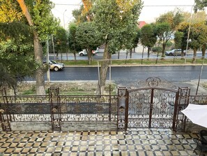 A terrace with a tiled floor, a wrought iron gate, and a view of a street with cars and trees. - Hotel LION Almaty (Almaty)