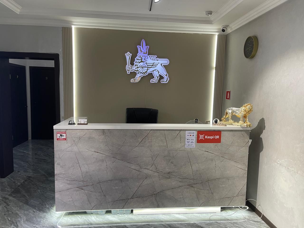 A reception desk with a marble top, a logo on the wall, and a golden lion statue.