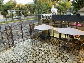 An outdoor seating area with a checkered floor, metal railing, and umbrellas. - Hotel LION Almaty (Almaty)