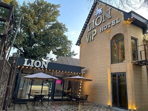 The exterior of the Lion Hotel with a brick facade, large windows, and outdoor seating area with umbrellas. - Hotel LION Almaty (Almaty)