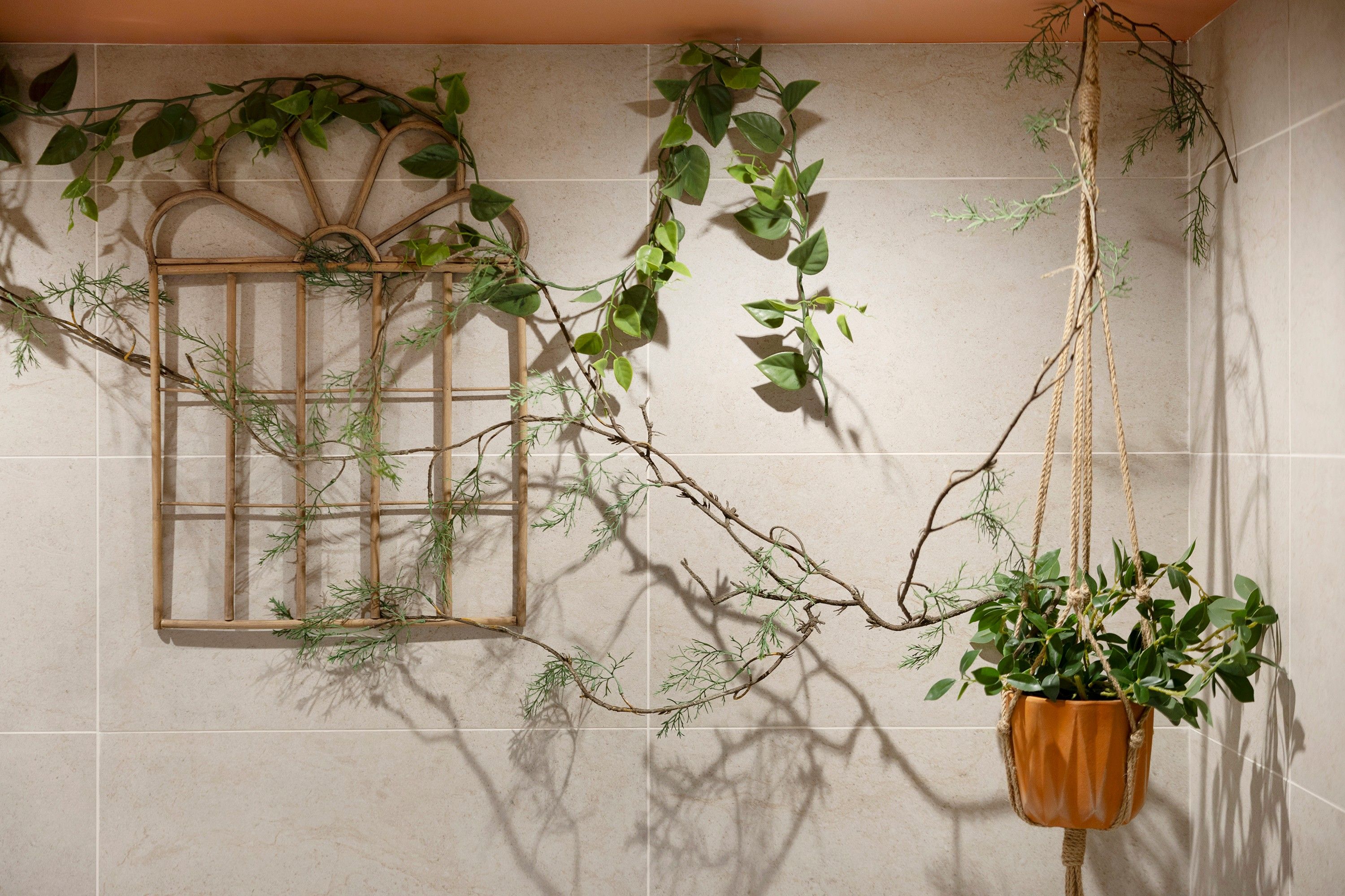 A room with a wooden trellis against a tiled wall, a hanging plant, and a window with a metal grille.
