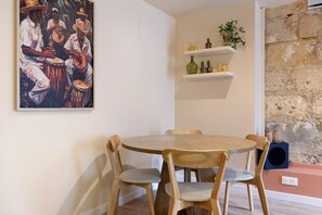 Un coin repas comprenant une table ronde en bois, quatre chaises en bois, un tableau accroché au mur et une étagère ornée d’objets décoratifs.