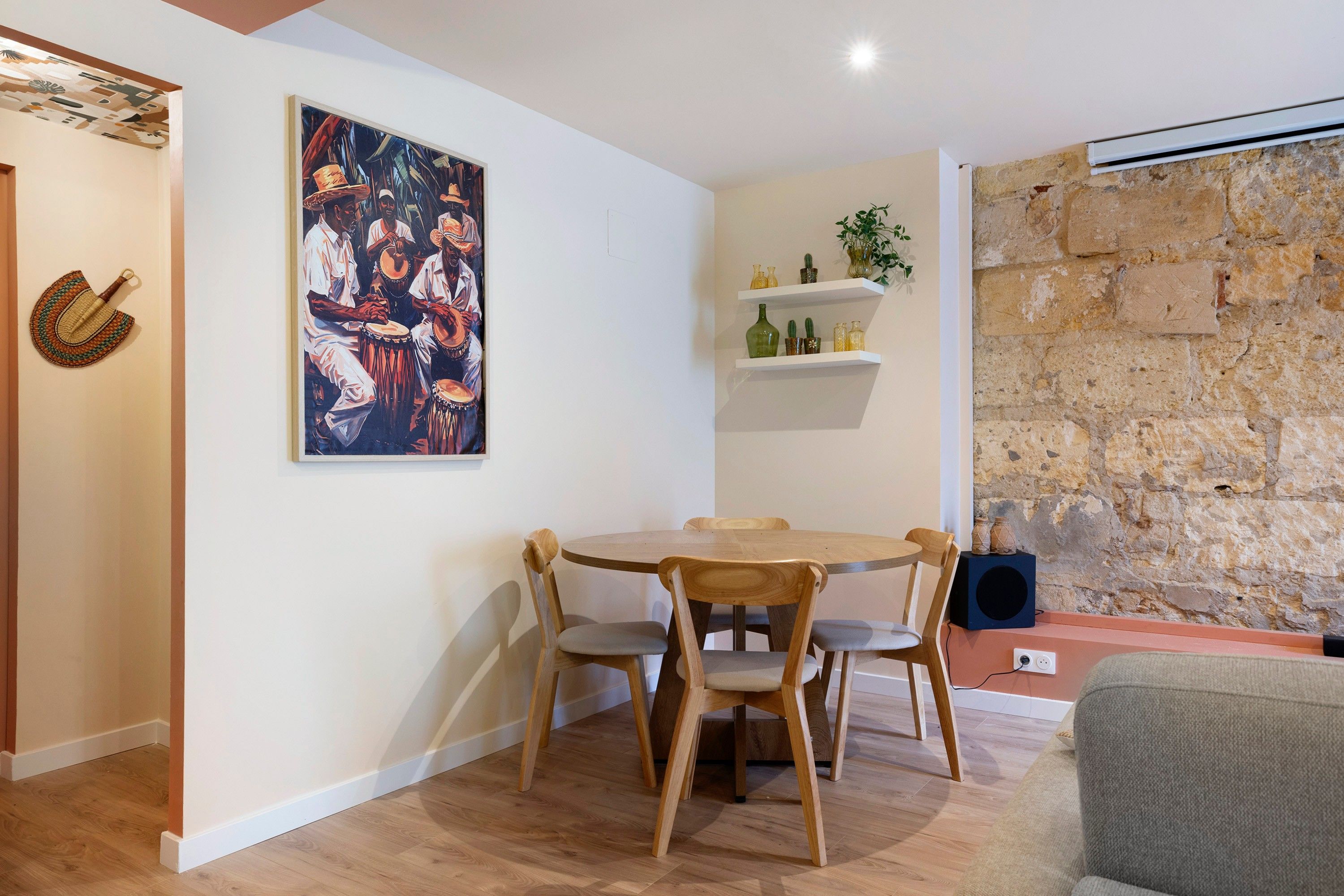 A dining area with a wooden table and chairs, a painting on the wall, and a stone wall.