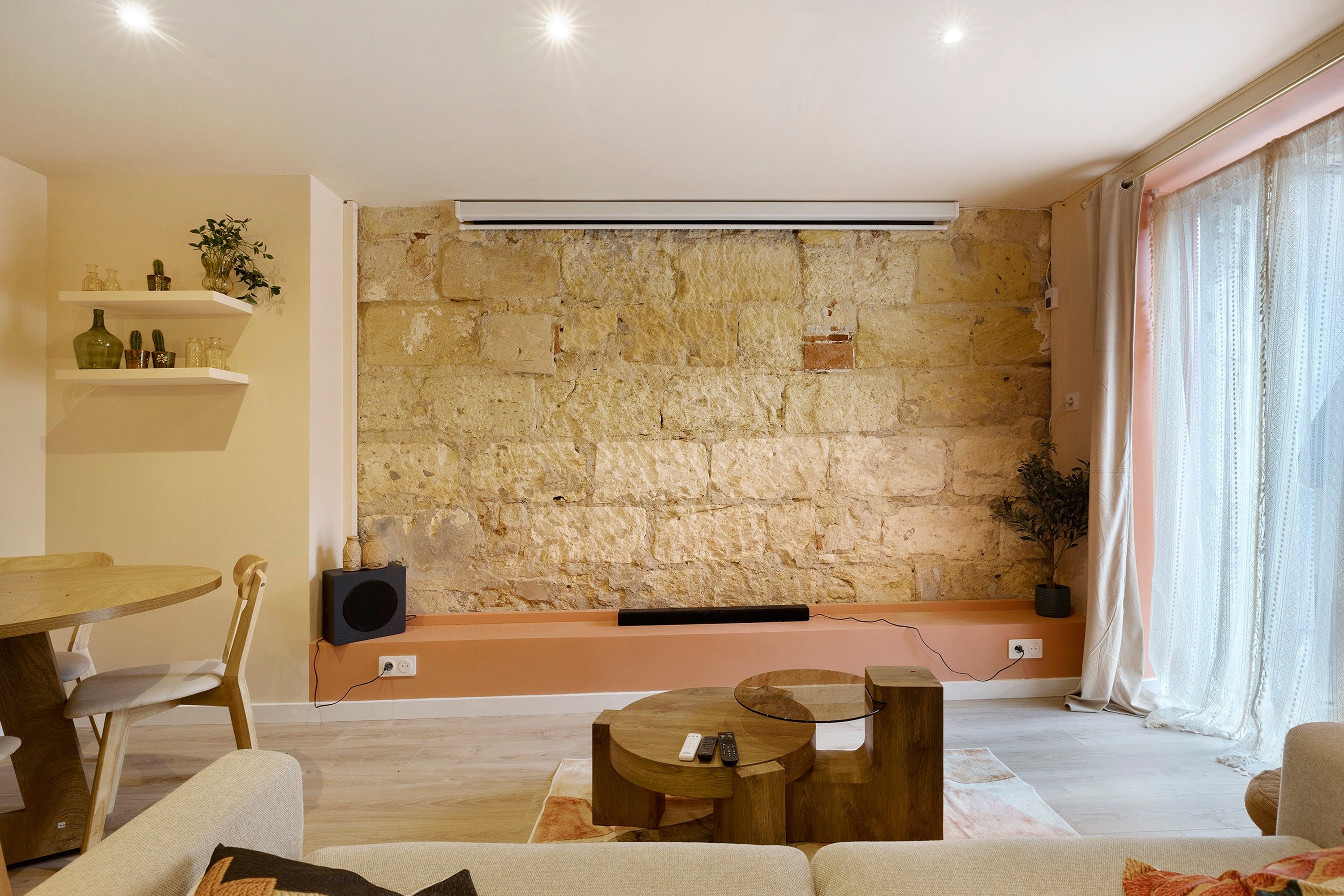 Un salon moderne avec un mur en pierre, une table basse ronde en bois, un canapé et un coin repas comprenant une table et des chaises.