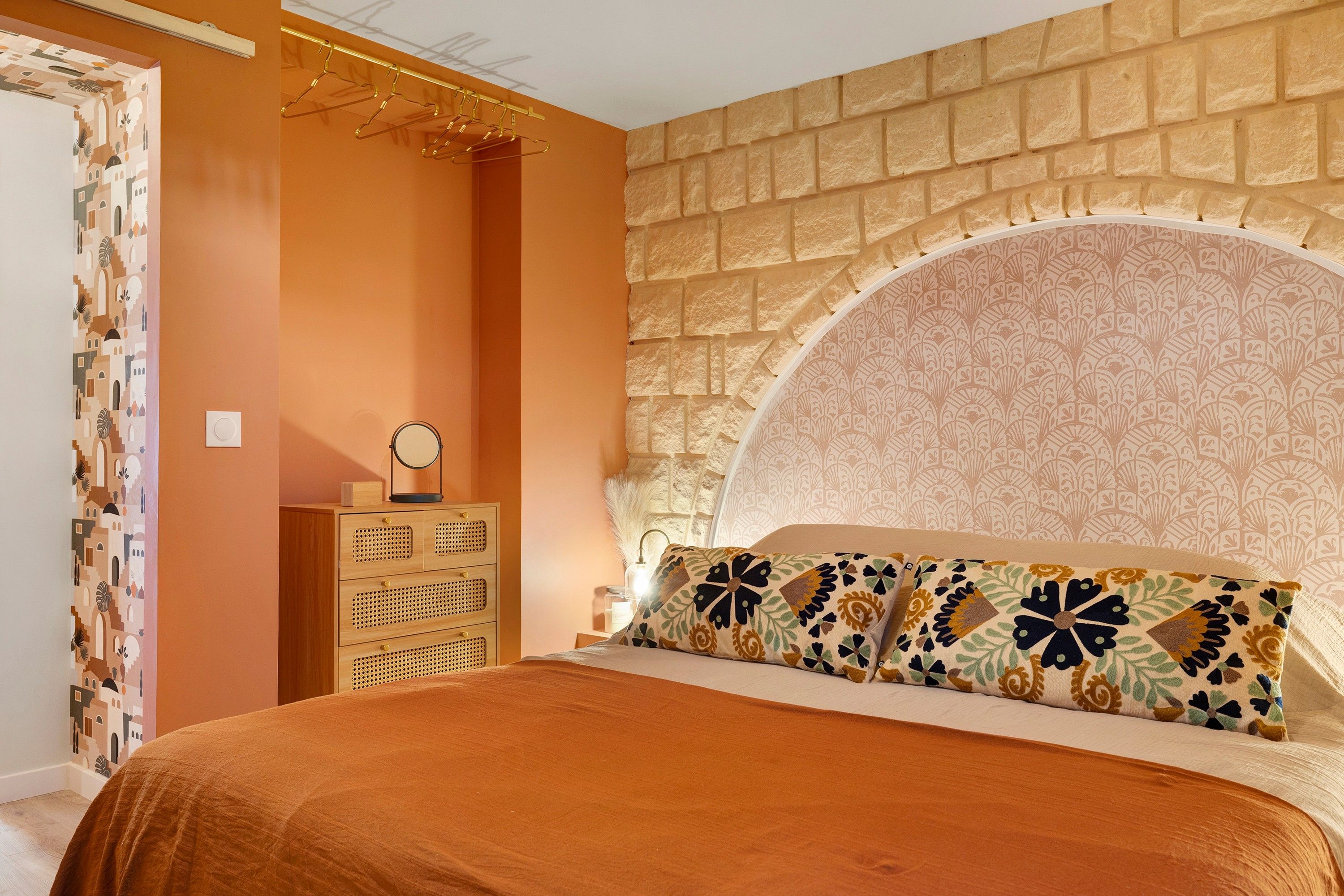 A bedroom with a bed, a dresser, a mirror, and a wall with a patterned design.