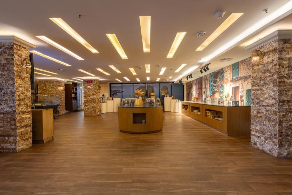Un vestíbulo de hotel con un mostrador de recepción central, suelo de madera y detalles de piedra en las paredes.