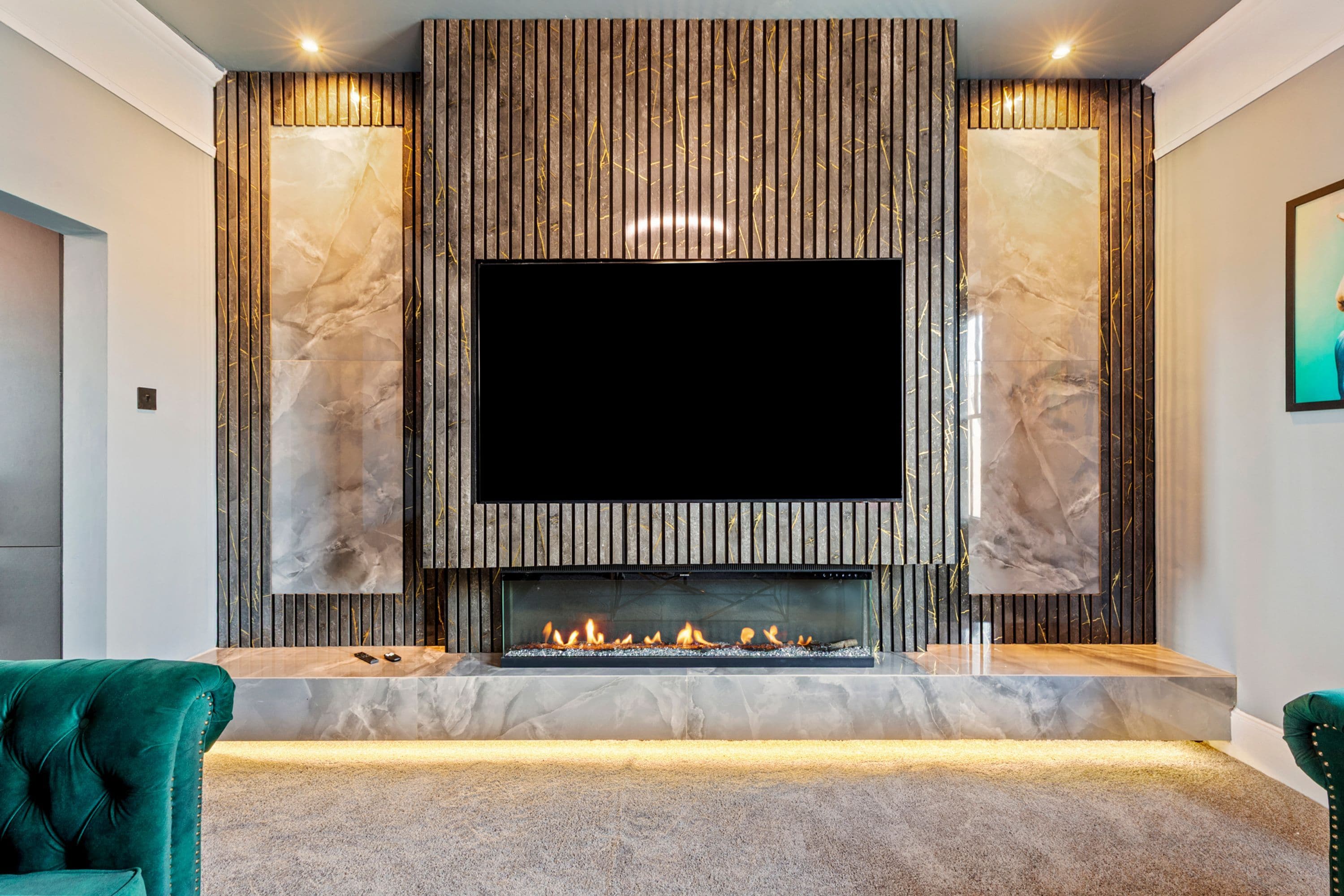 Una sala de estar moderna con un televisor de pantalla plana grande montado sobre una chimenea, flanqueada por paneles de mármol, y que presenta un sillón verde mullido.